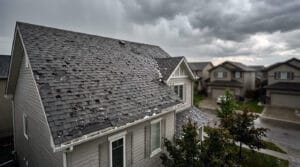 Impact‑resistant asphalt shingle roof on a Calgary suburban home showing visible hail damage and remaining hailstones after a severe summer storm.